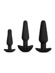 The 3 plugs from the b-Vibe Anal Training & Education Butt Plug Set in Black are shown against a blank background. The plugs are tapered with thin necks and flared, curved bases. They are arranged with the smallest on the left and largest on the right.