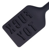 A closeup of the top end of the black silicone paddle. The words "FUCK TOY" are inscribed backwards in the surface. 