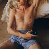A man reclining on a pillow, shirtless and wearing boxers. In one hand he has the Sub One vibrator. 