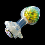 A butt plug made of transparent PVC lying on a black background. The surface has an iridescent sheen, while the head is filled with yellow and blue glitter. 