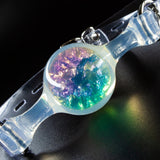 Close-up of a transparent PVC ball gag, showing the glittery purple, yellow, and green materials inside the ball. 