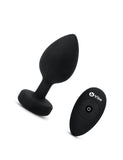 The b-Vibe Vibrating Jewel Butt Plug is shown against a blank background next to its 4 buttoned remote. The plug is a size 2XL, which is Black colored.
