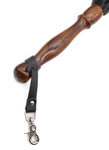 A close up image of the Sissoo Rosewood Long Handle Leather Flogger on a white background. Shown is the included leather hanger strap with crab-claw hook attached to the handle of the flogger.